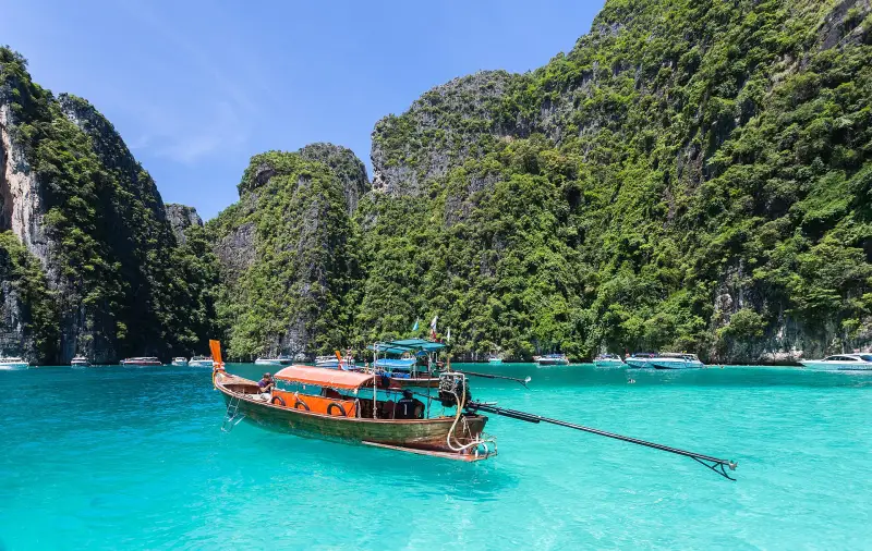 Long-tail boat in turquoise water beside limestone cliffs of Phi Phi Islands, Thailand