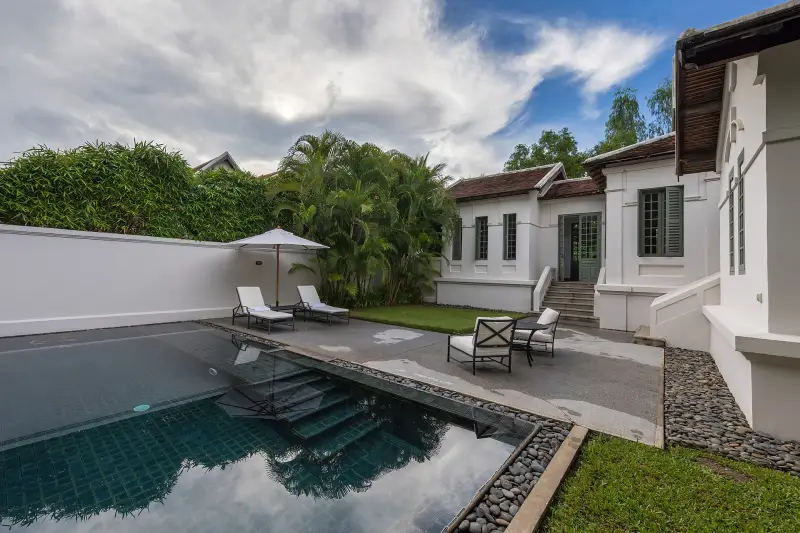 Resort swimming pool with sun loungers beside a colonial-style building